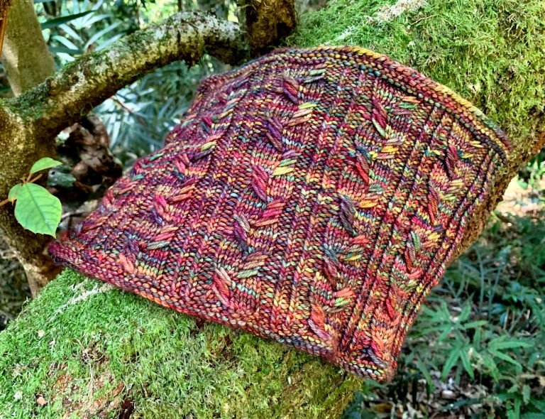 Cowl made from the Next Chapter knitting pattern placed on a log covered in moss