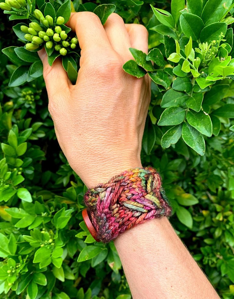 A hand holds floral buds. A knitted cuff made from the Next Chapter Cuff is on her wrist